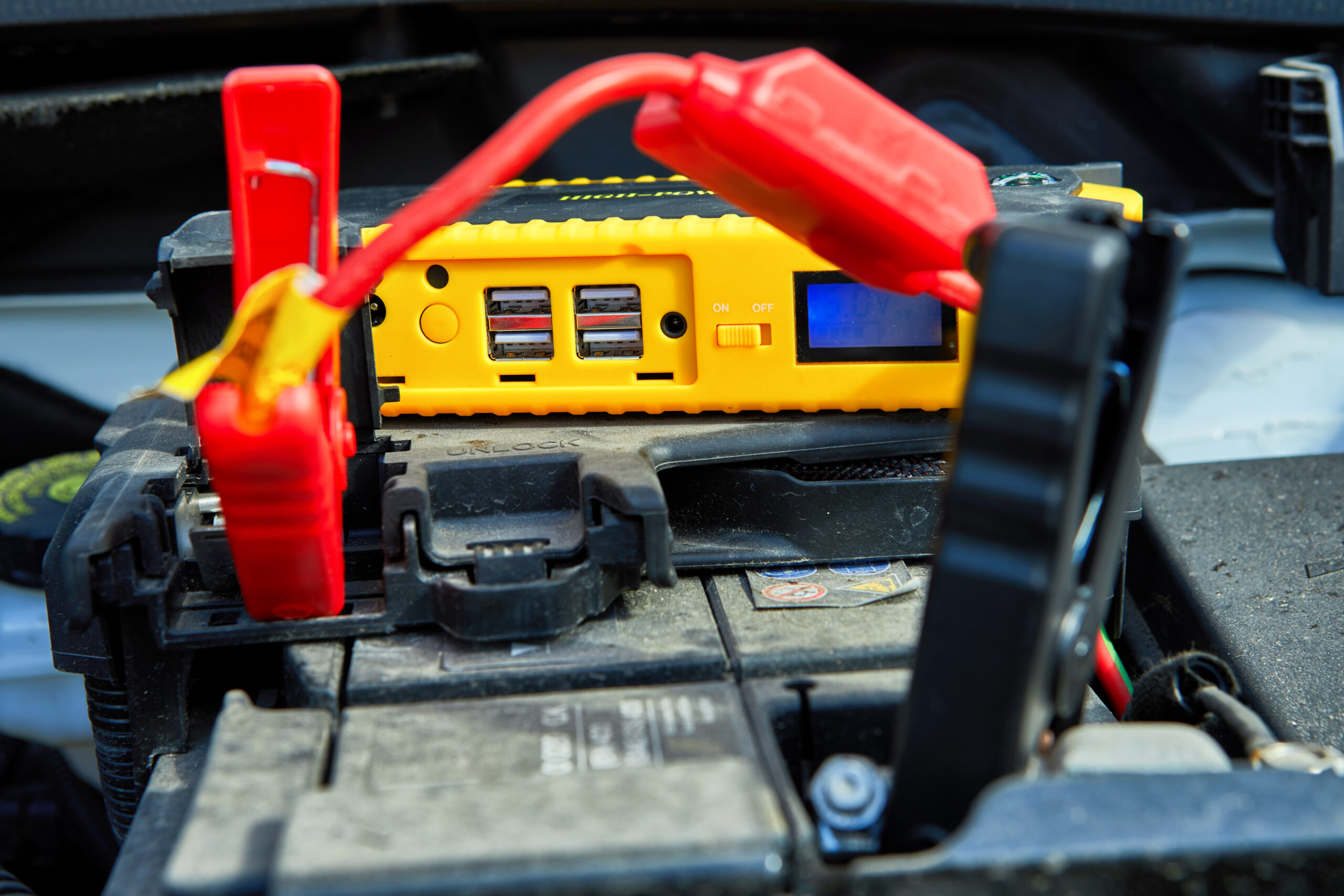 Een auto-accu wordt opgeladen met startkabels en een draagbare jumpstarter.